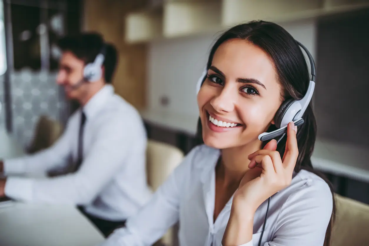 Two people wearing telephone headsets taking calls at desks in an open-plan office.
